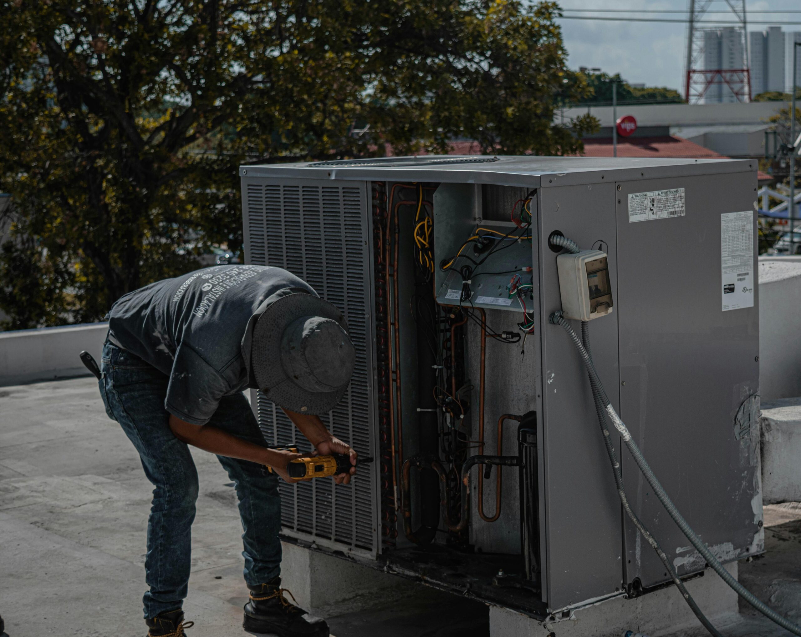 A technician is repairing an air conditioning unit on a rooftop, demonstrating skilled manual work.