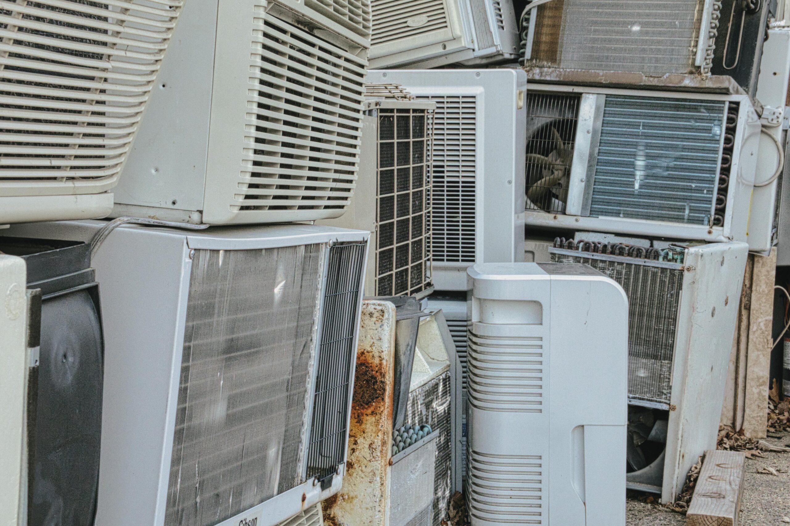 A collection of various old and broken air conditioning units piled outdoors.